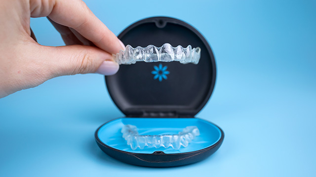 An image of a hand holding an open dental impression tray with a blue background, showcasing the transparent plastic mold used for creating dental impressions.